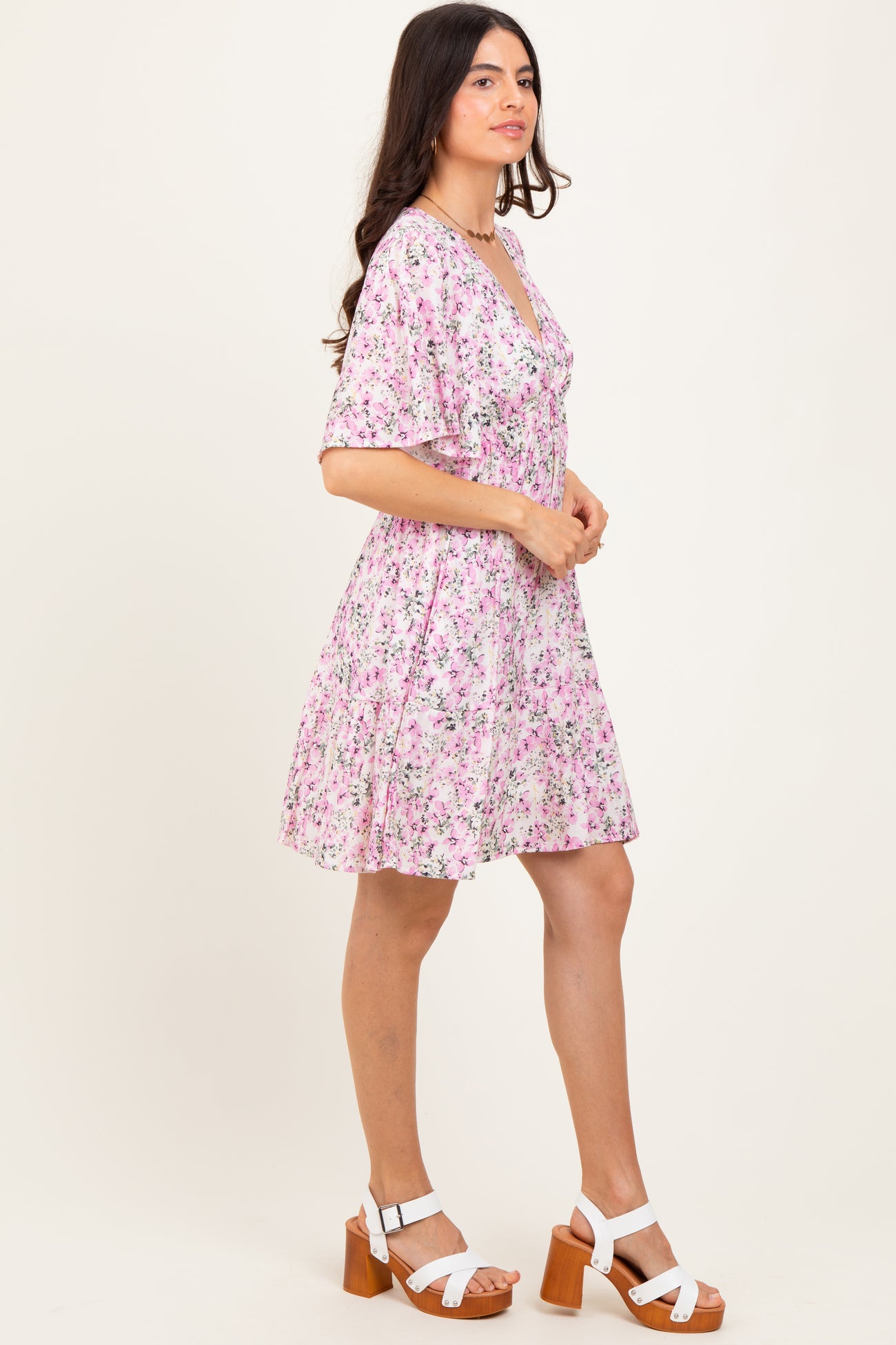 woman wearing a pink floral short sleeve dress with a v-neck and flared hem, paired with white heeled sandals