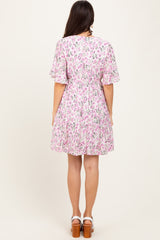 woman wearing a pink floral short sleeve dress with a tiered skirt, standing with her back to the camera