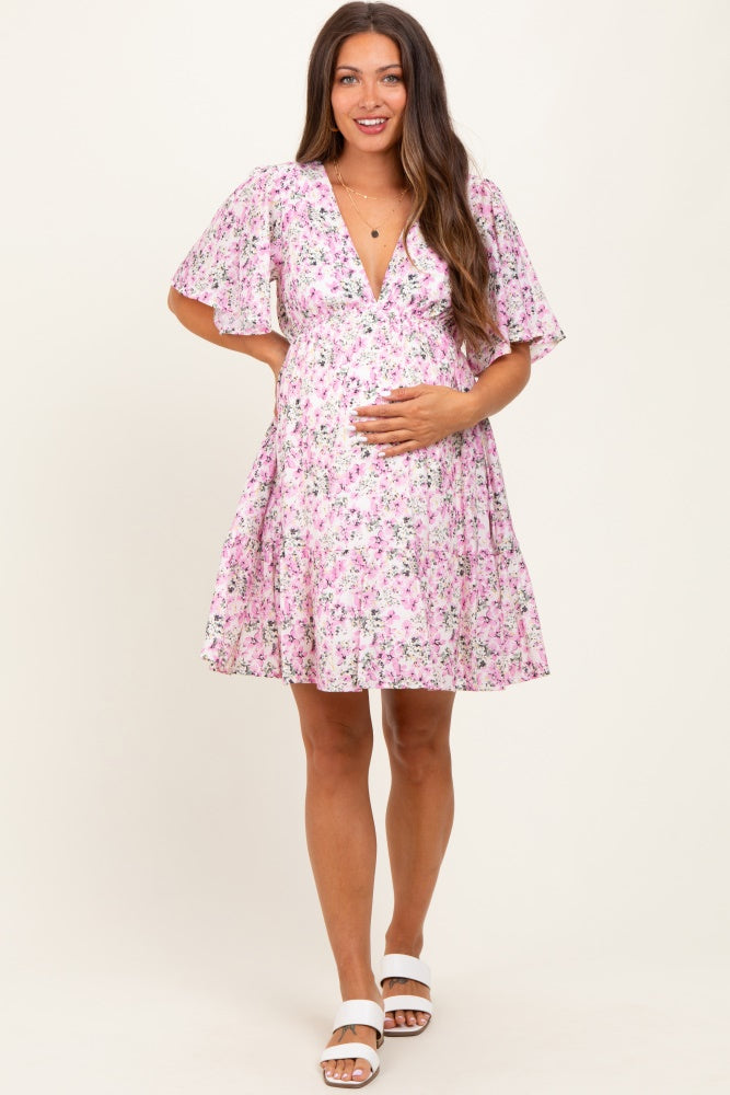 woman wearing a pink floral maternity dress with flutter sleeves and holding her baby bump