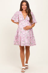woman wearing a pink floral maternity dress with flutter sleeves and holding her baby bump