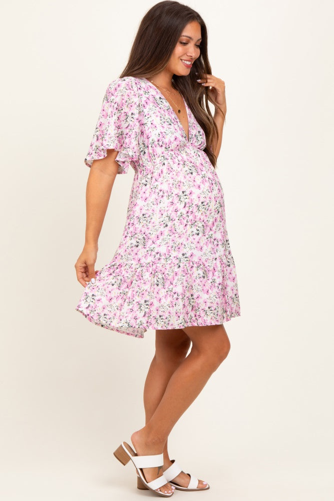 woman wearing a pink floral maternity dress with flutter sleeves and a ruffled hem, showcasing her baby bump