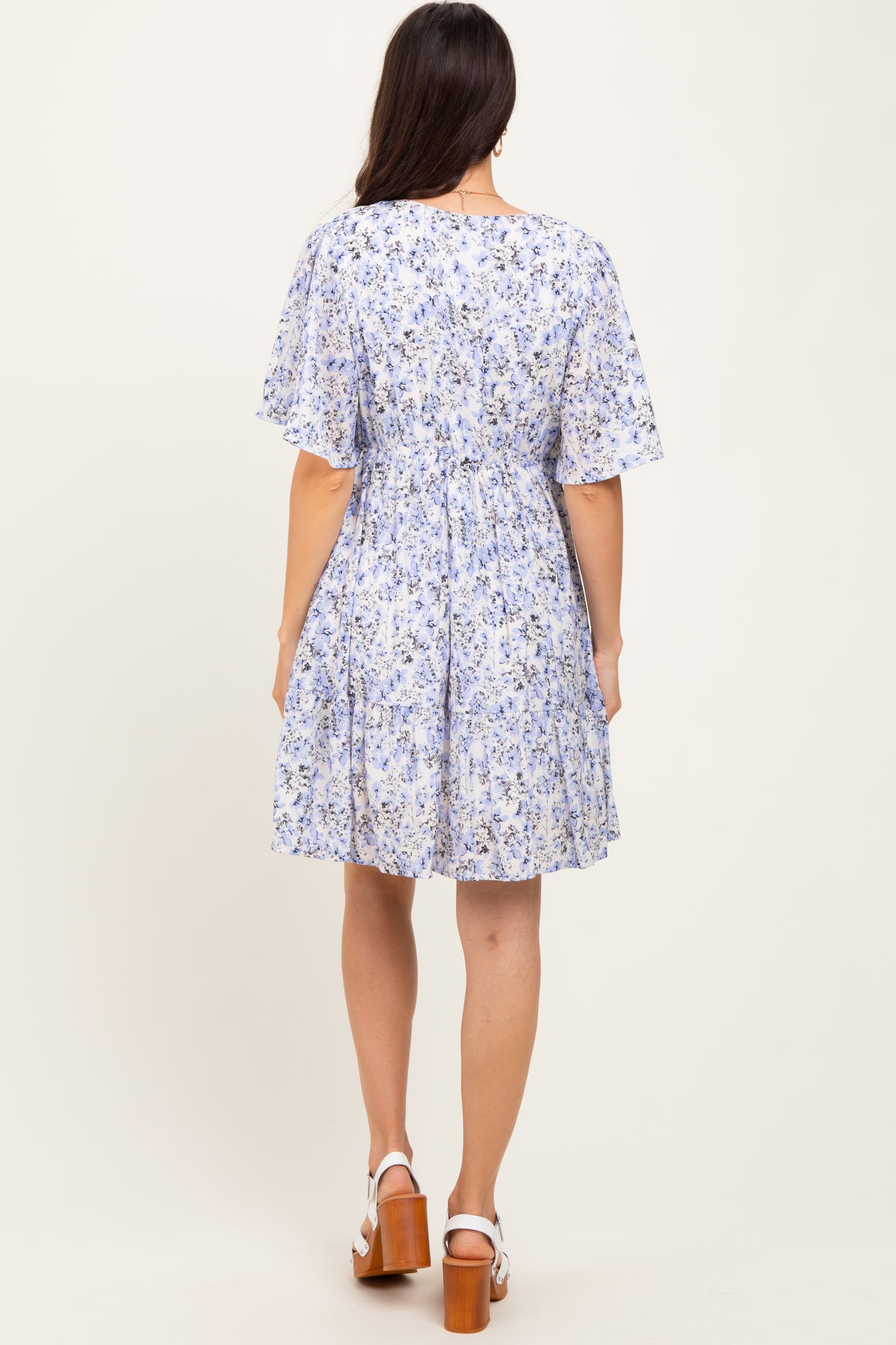 woman wearing a back view of a light blue floral print short sleeve dress with a cinched waist and flowy skirt