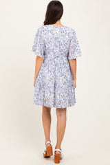 woman wearing a back view of a light blue floral print short sleeve dress with a cinched waist and flowy skirt