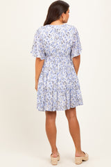 woman wearing a flowy blue floral maternity dress with short flutter sleeves and a tiered skirt, showing her baby bump from the back