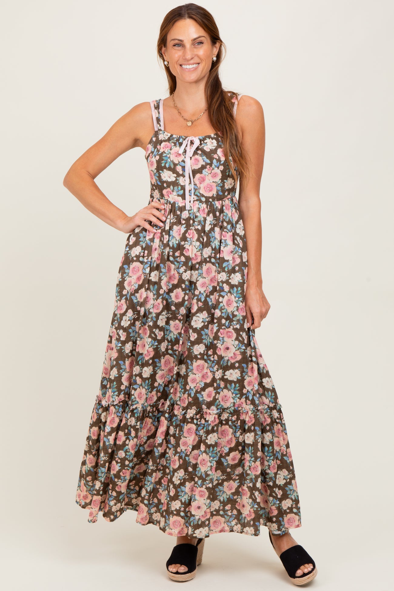 woman wearing a floral print maxi dress with thin straps and tiered ruffles, posing confidently