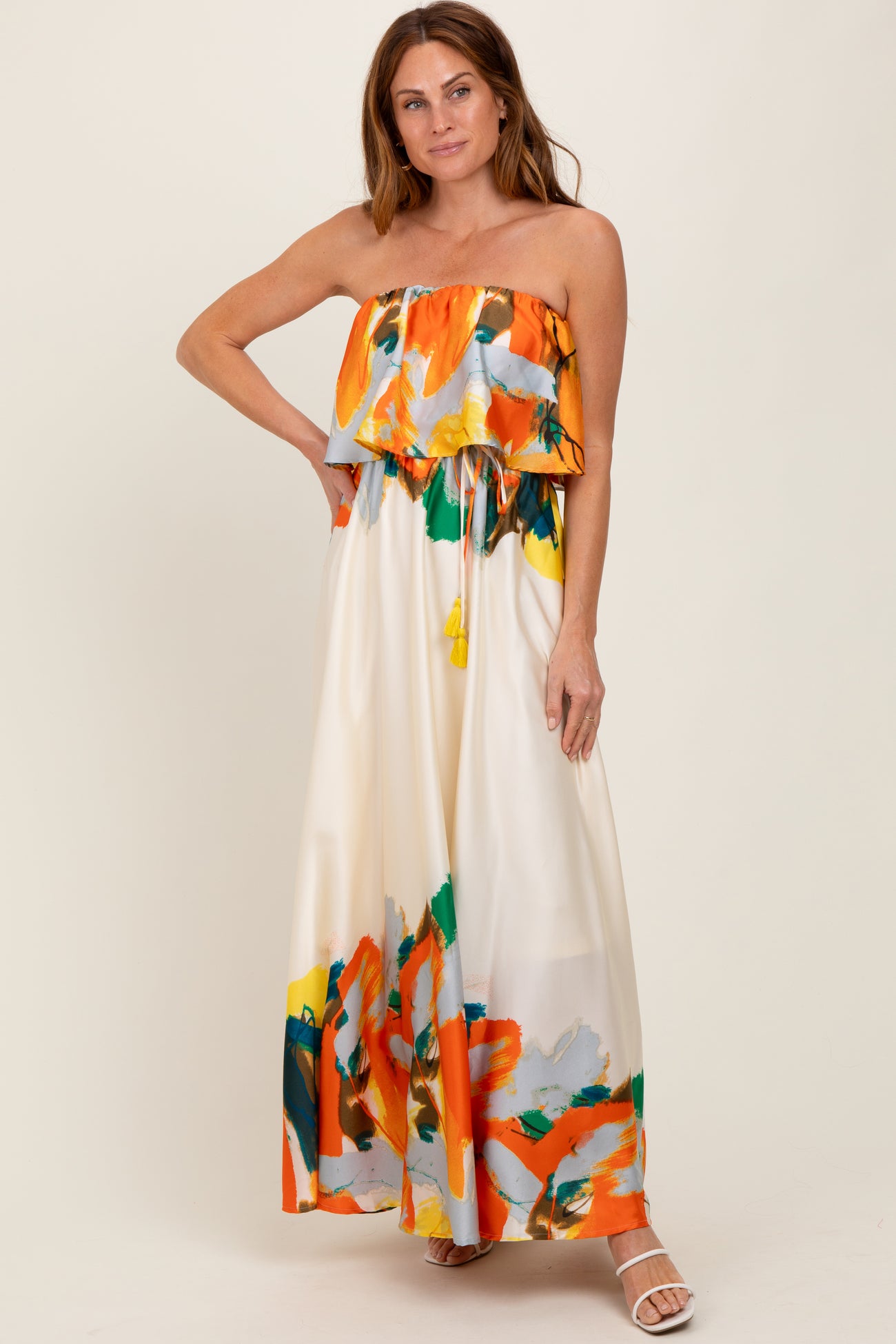 woman wearing a strapless floral maxi dress with a ruffled bodice and a drawstring waist in bright orange and green hues