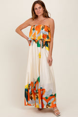 woman wearing a strapless floral maxi dress with a ruffled bodice and a drawstring waist in bright orange and green hues