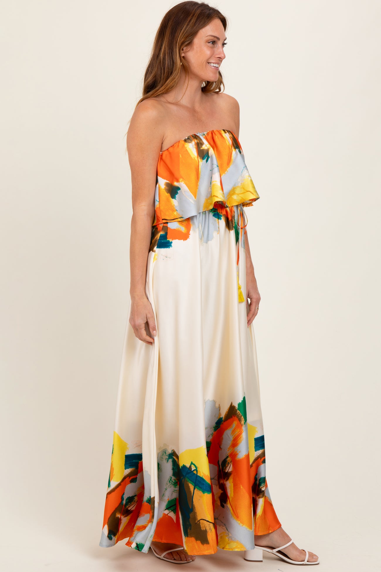 woman wearing a strapless colorful maxi dress with a ruffled top and an art-inspired design in vibrant hues