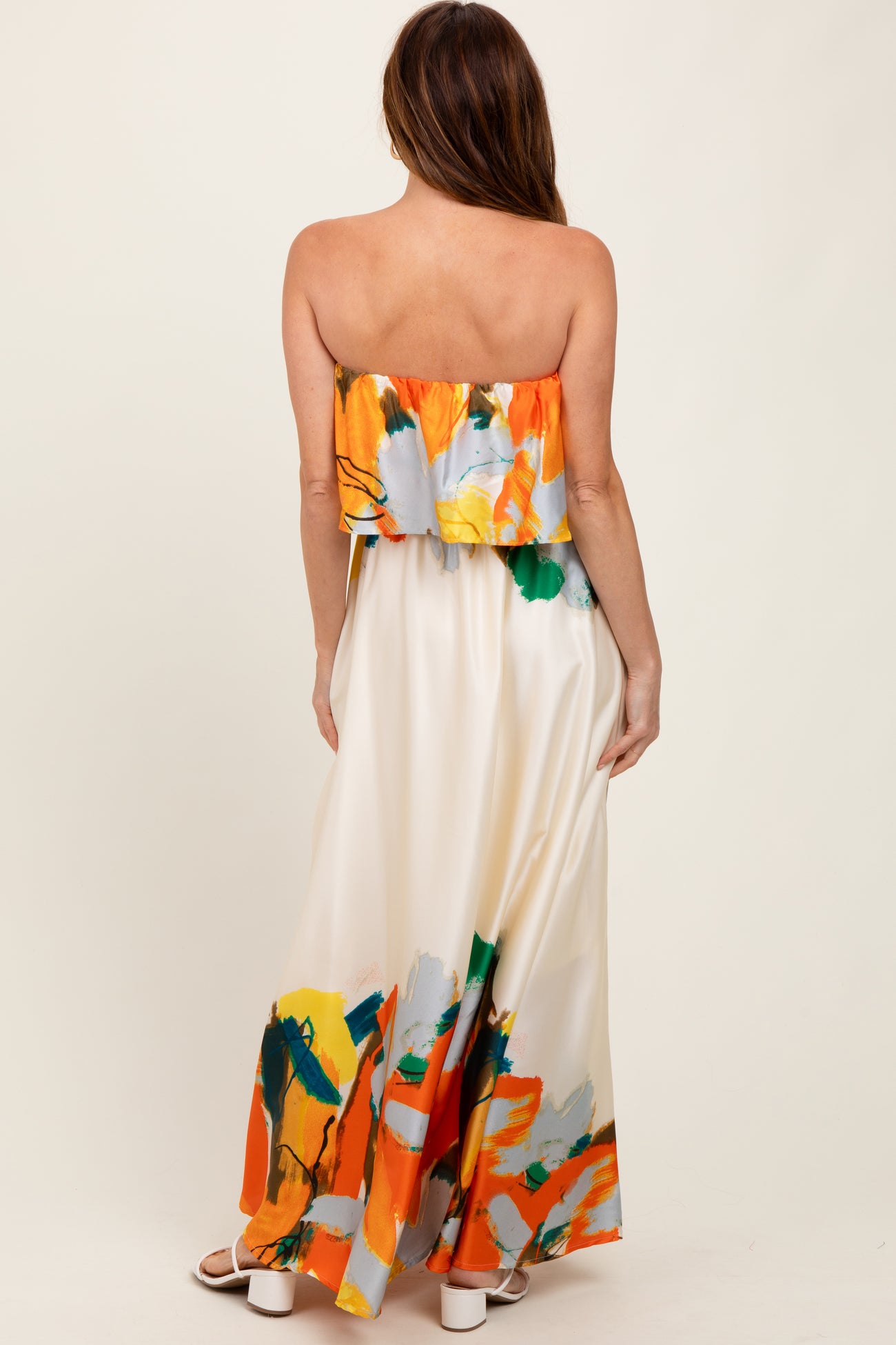woman wearing a strapless maxi dress with a colorful abstract print in orange, green, and yellow