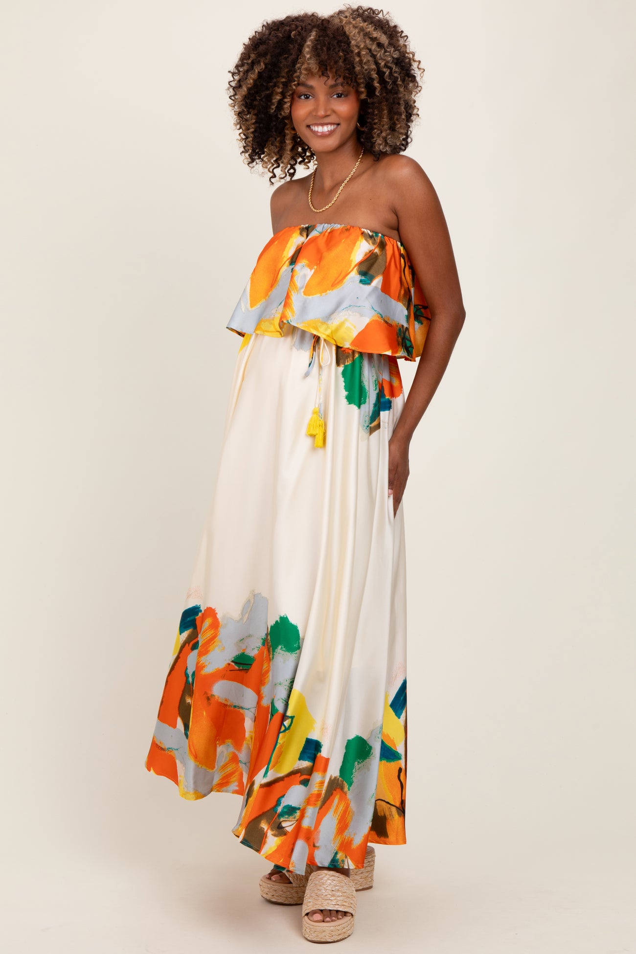 woman wearing a strapless floral maxi dress in orange, green, and yellow patterns, showcasing a baby bump