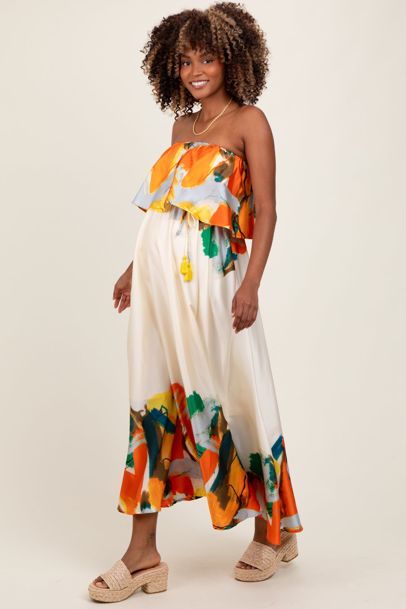 woman wearing a colorful strapless maternity dress with a ruffled overlay and a flowy skirt, showing a baby bump