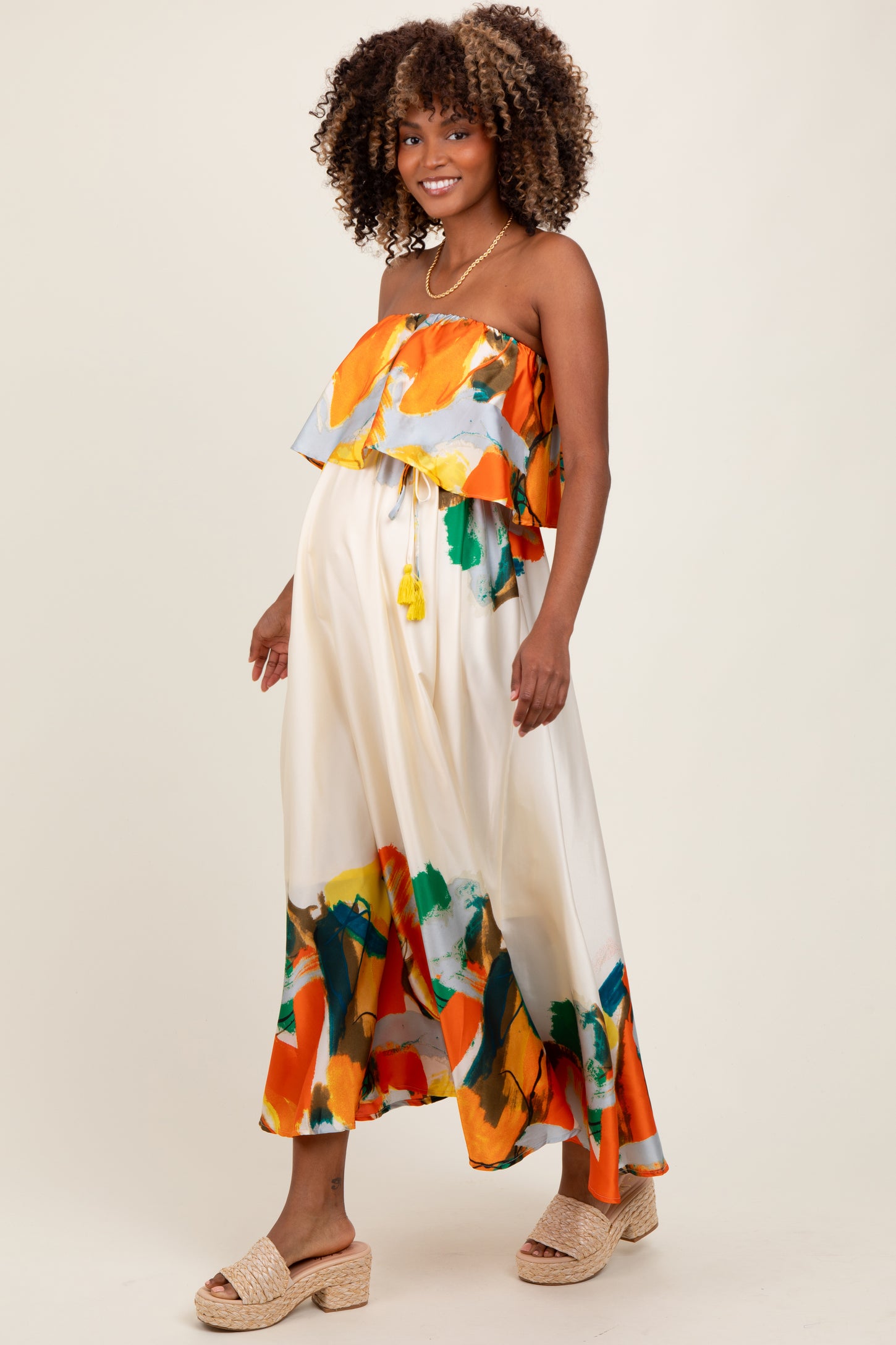 woman wearing a colorful strapless maternity dress with a ruffled overlay and a flowy skirt, showing a baby bump