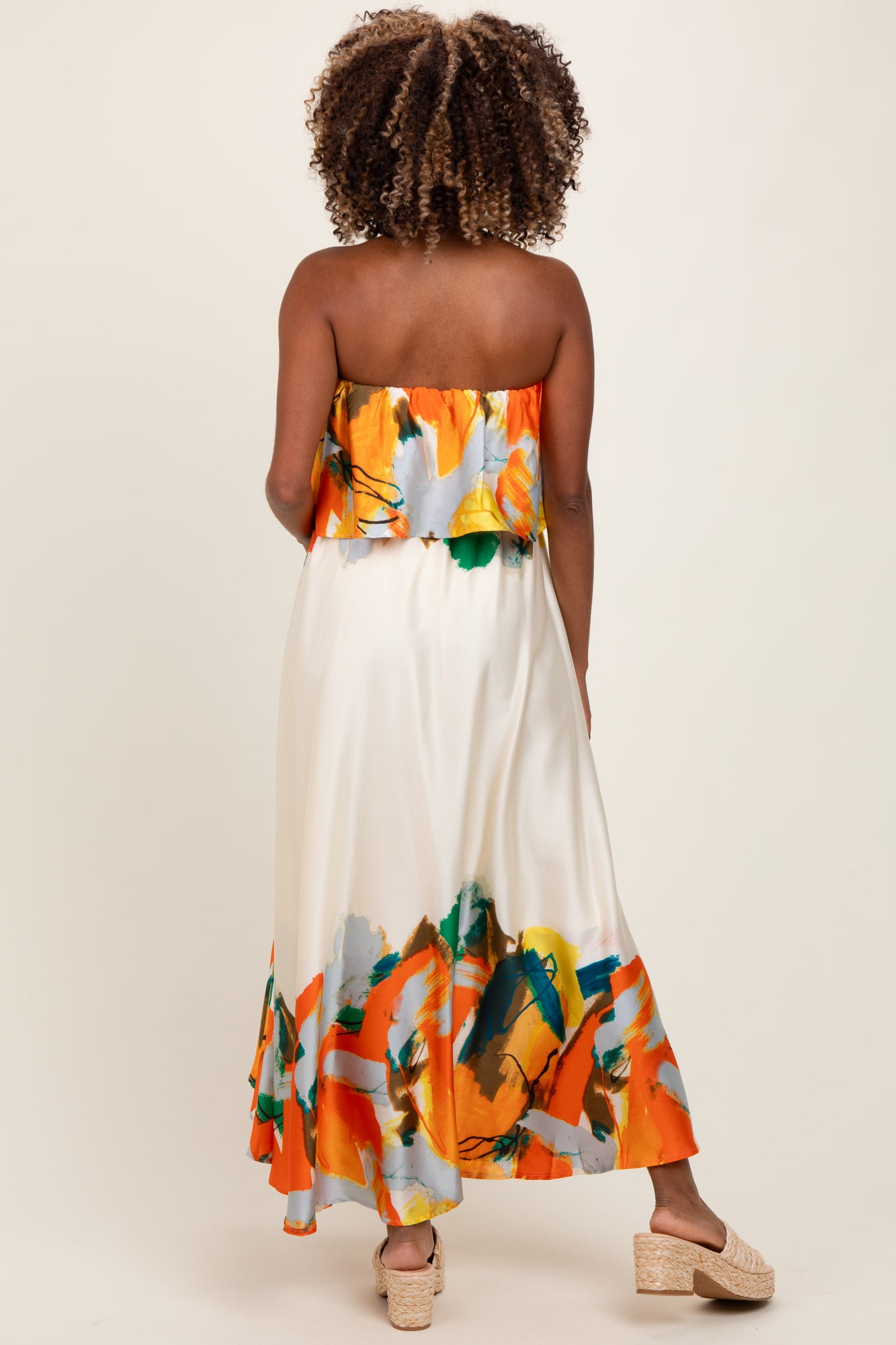 woman wearing a strapless floral patterned maternity dress in orange, green, and cream with a flowing silhouette