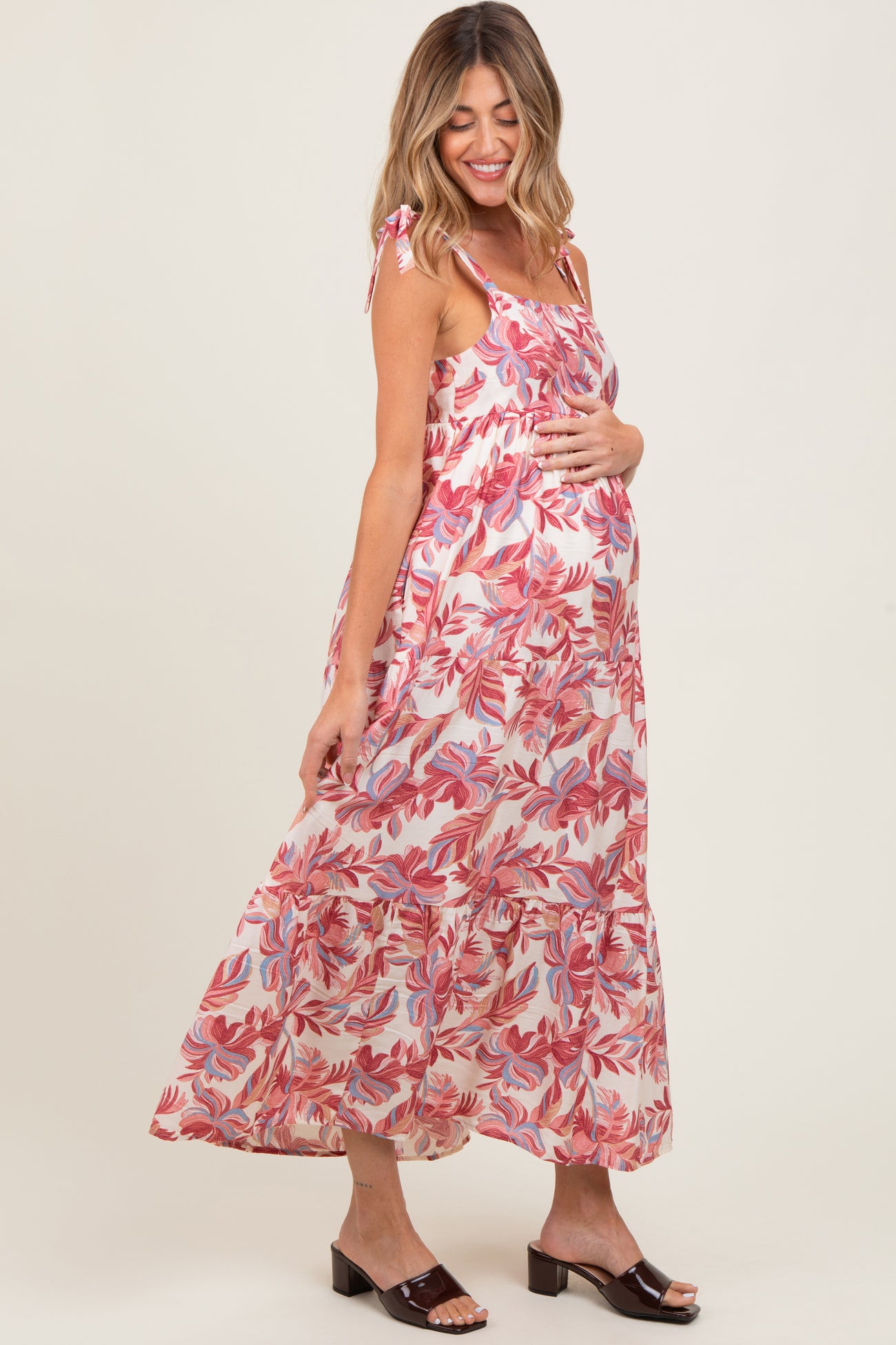 woman wearing a flowy pink and white floral maternity maxi dress, gently cradling her baby bump