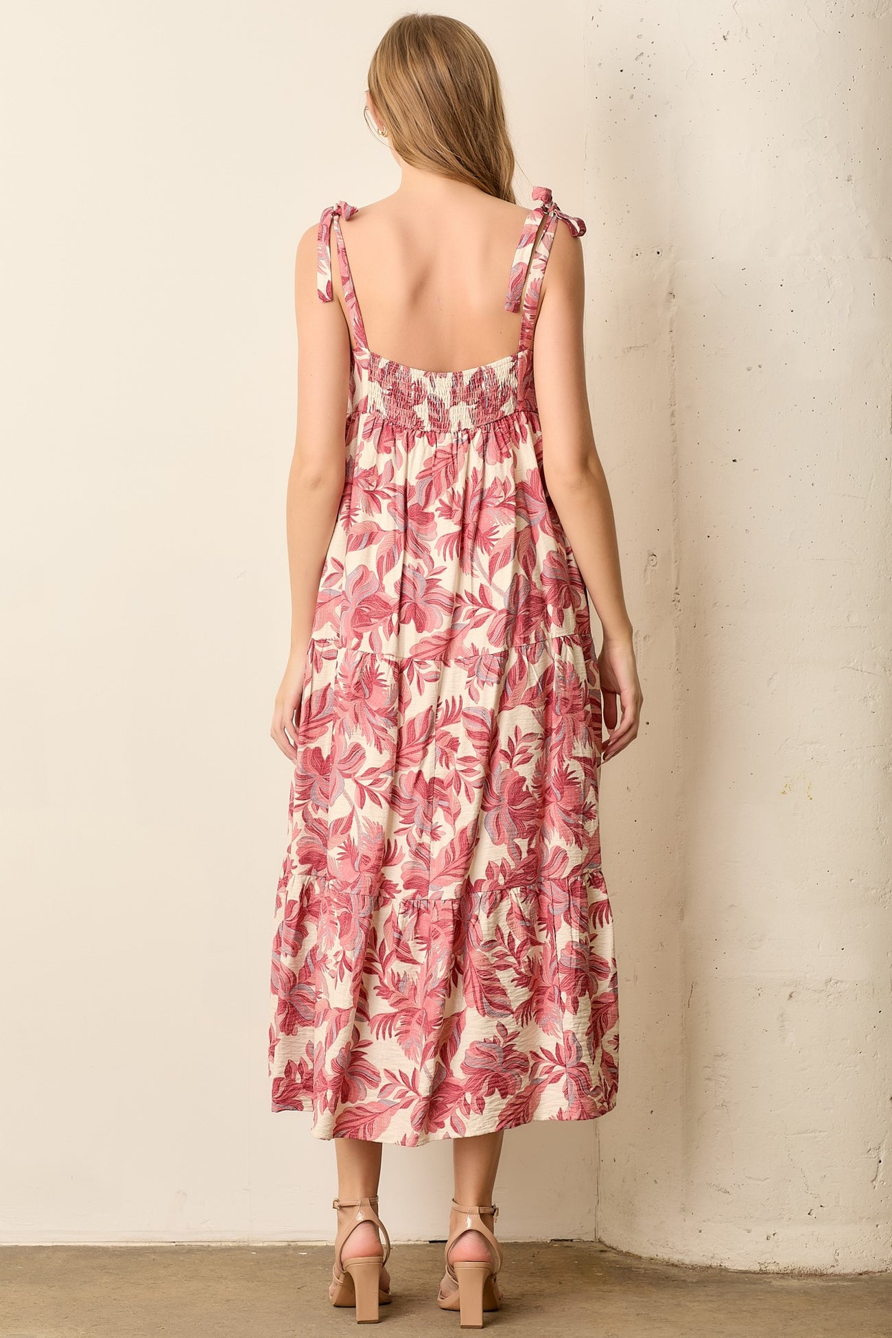 woman wearing a back view of a floral midi dress with tie straps and a smocked bodice in pink and cream tones