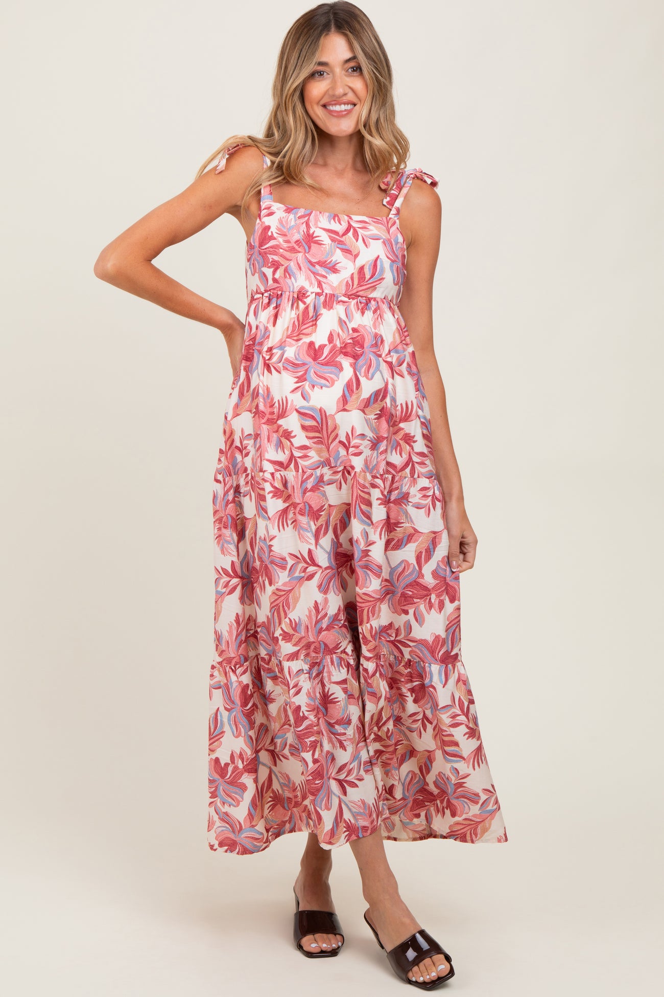 woman wearing a floral print maternity maxi dress with tie straps and a flowy skirt, smiling and posing