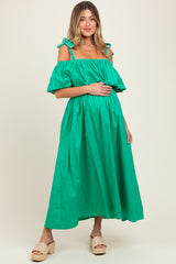 woman wearing a bright green off-the-shoulder maternity dress with ruffle details and holding her baby bump