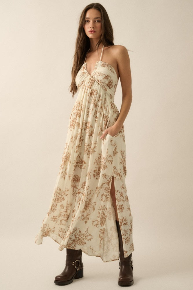 woman wearing a cream floral maxi dress with a halter neckline and side slits, paired with brown heeled boots