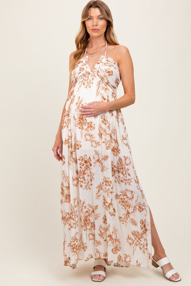 woman wearing a floral print maternity maxi dress with a halter neckline, gently holding her baby bump