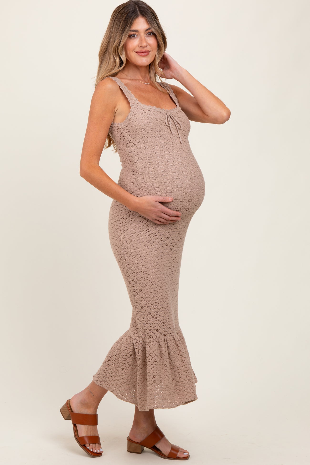 woman wearing a beige knitted maternity dress with a flared hem and holding her baby bump
