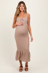 woman wearing a beige ribbed maternity dress with a tie detail and ruffled hem, holding her baby bump.