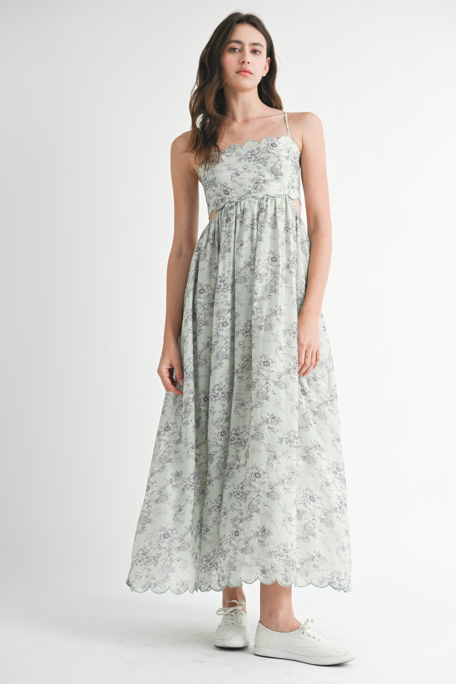 woman wearing a light green floral maxi dress with spaghetti straps and a cinched waist, paired with white sneakers