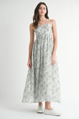 woman wearing a light green floral maxi dress with spaghetti straps and a cinched waist, paired with white sneakers