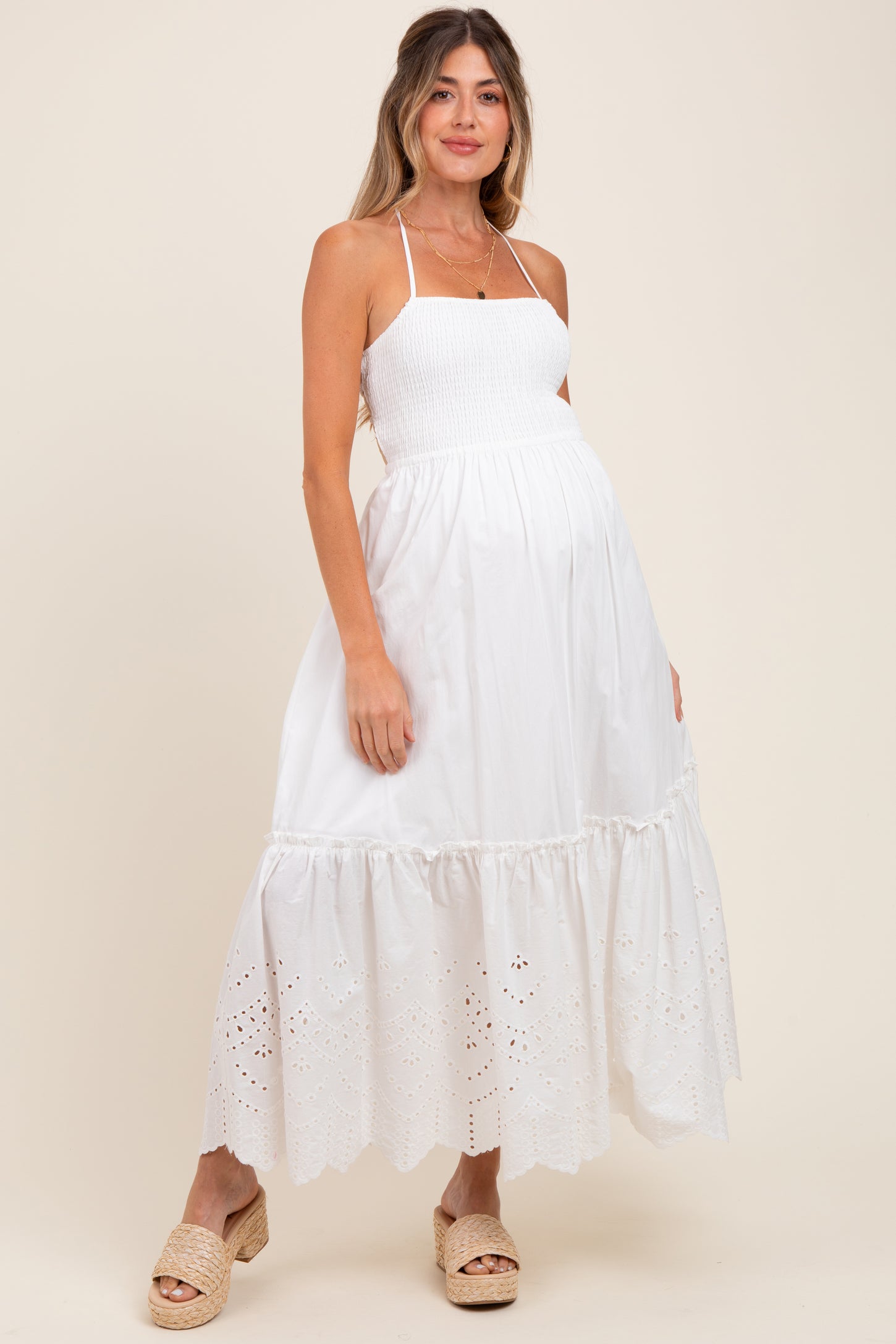woman wearing a white maternity maxi dress with smocked bodice and eyelet hem, showing her baby bump