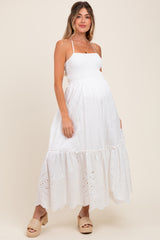 woman wearing a white maternity maxi dress with smocked bodice and eyelet hem, showing her baby bump