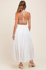 woman wearing a white maternity maxi dress with a halter neckline and eyelet detailing on the lower hem