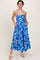 woman wearing a blue floral maxi dress with spaghetti straps and pockets, standing and smiling