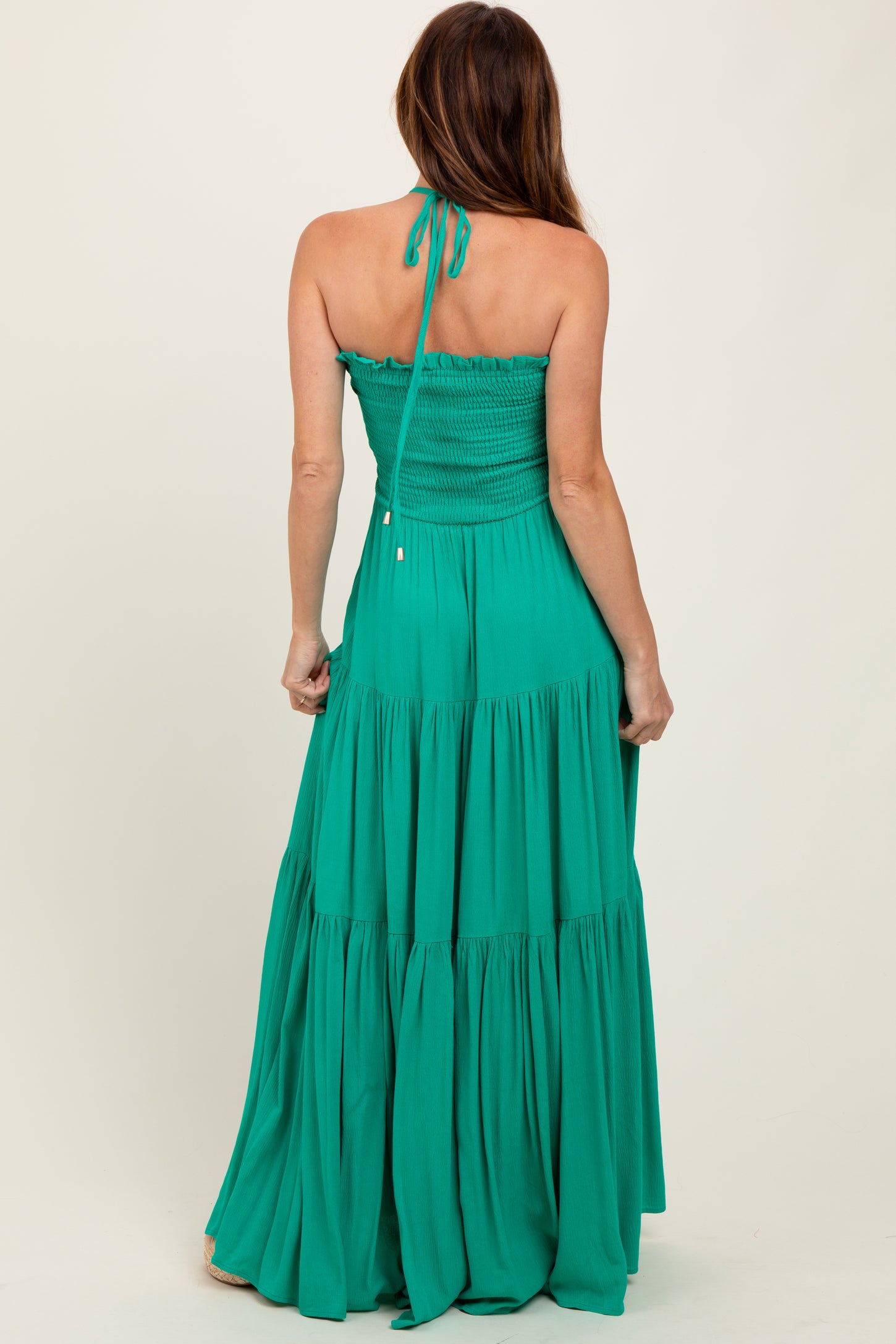 woman wearing a strapless green maxi dress with a smocked bodice and tiered skirt, seen from the back