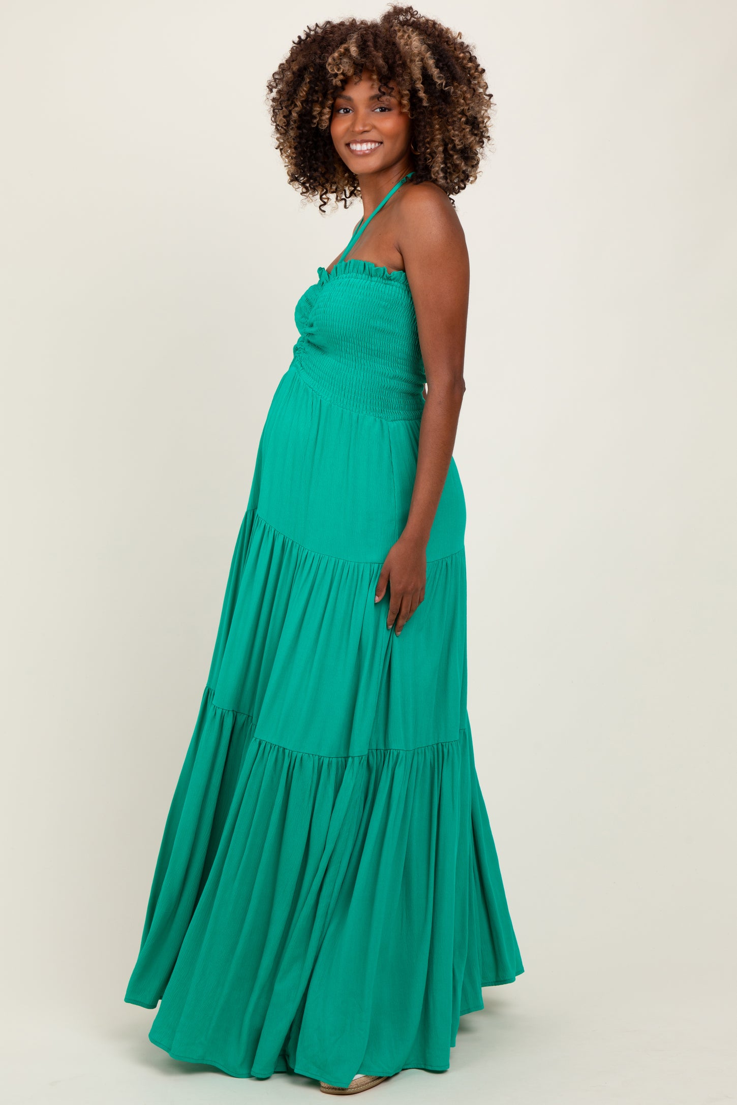 woman wearing a green maternity maxi dress with smocked bodice and tiered skirt, showing her baby bump
