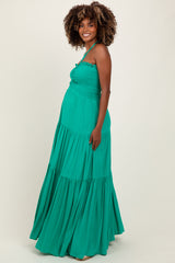 woman wearing a green maternity maxi dress with smocked bodice and tiered skirt, showing her baby bump
