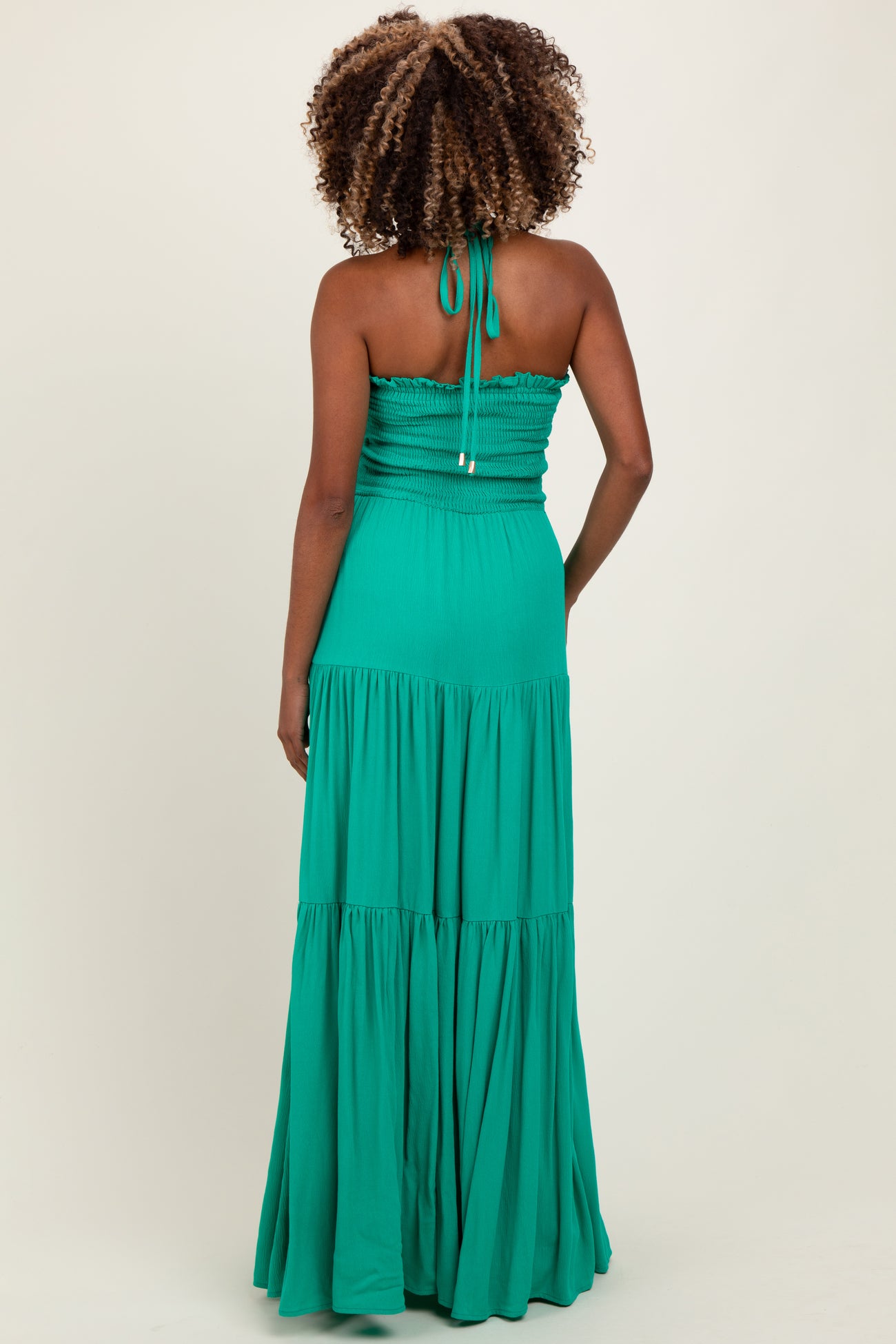 woman wearing a green maternity maxi dress with a smocked bodice and tiered skirt, showing off her baby bump from the back