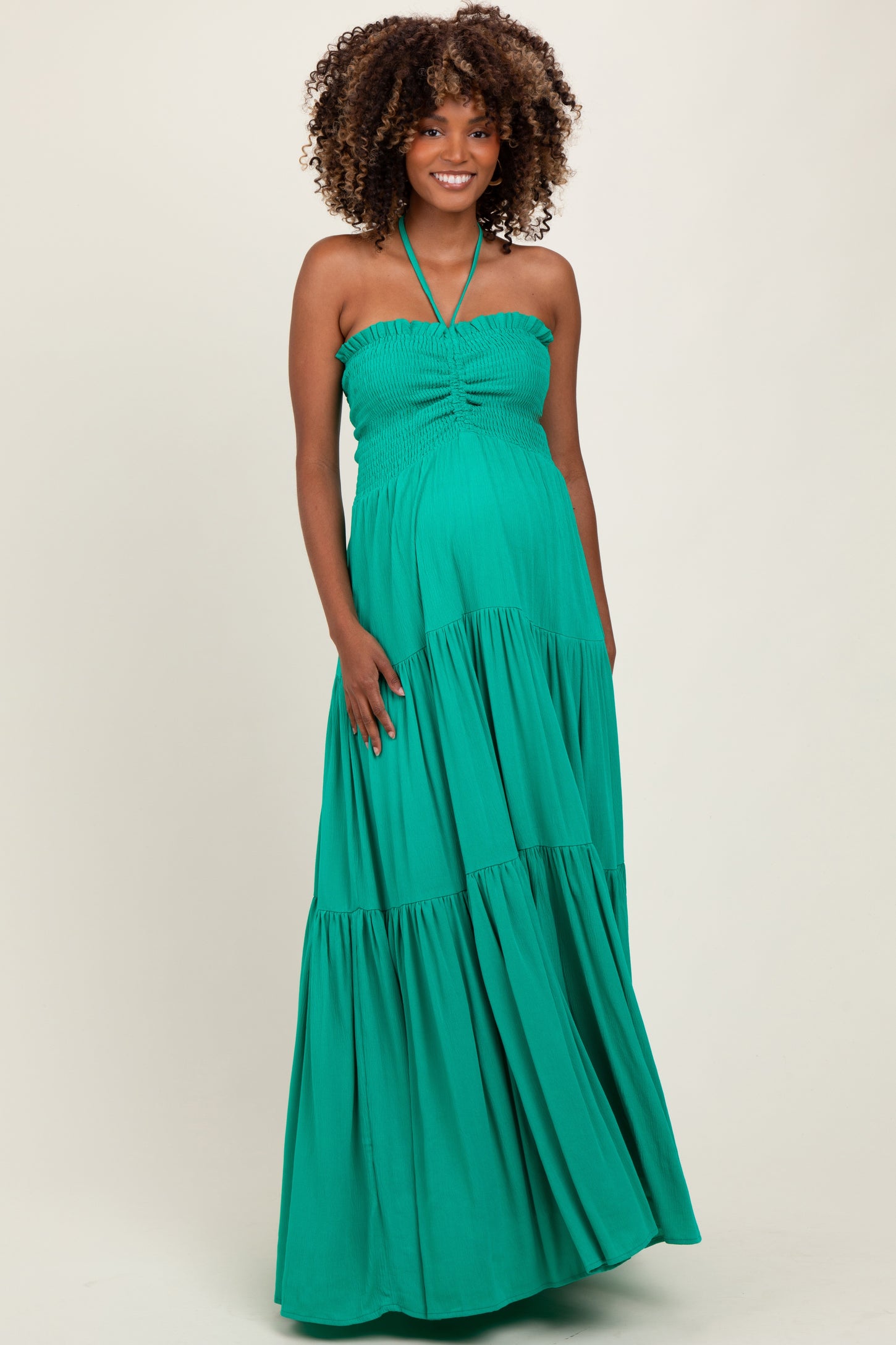 woman wearing a green strapless maternity maxi dress with a halter neck and a flowing tiered skirt, showcasing her baby bump