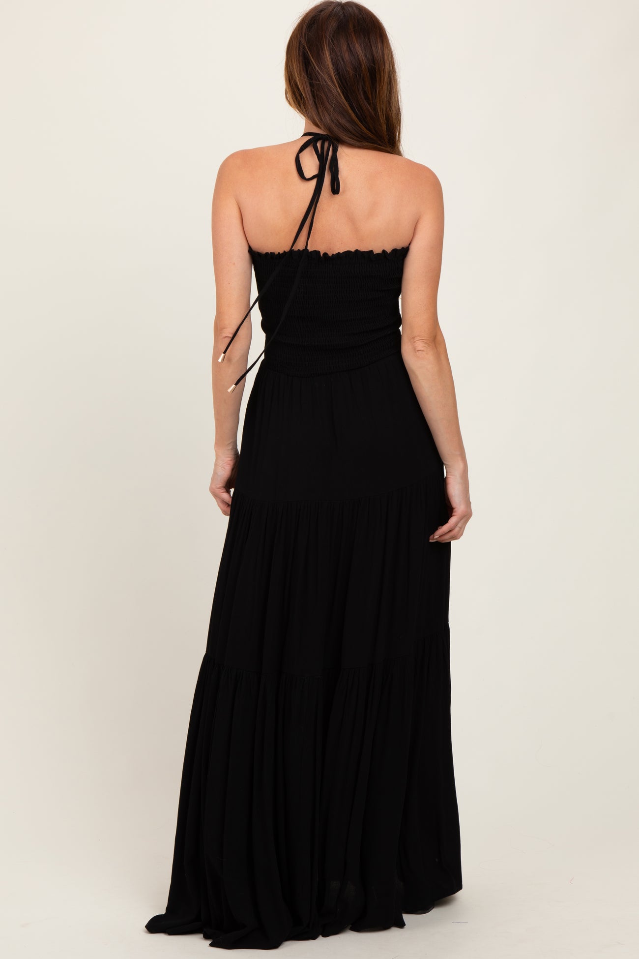 woman wearing a black strapless maxi dress with a smocked bodice and tiered skirt, seen from the back