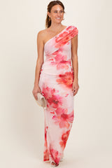 woman wearing a one-shoulder floral maxi dress in shades of pink and white, styled with a small clutch handbag