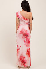 woman wearing a one-shoulder floral print maternity gown with pink and coral hues, showing her baby bump from the back