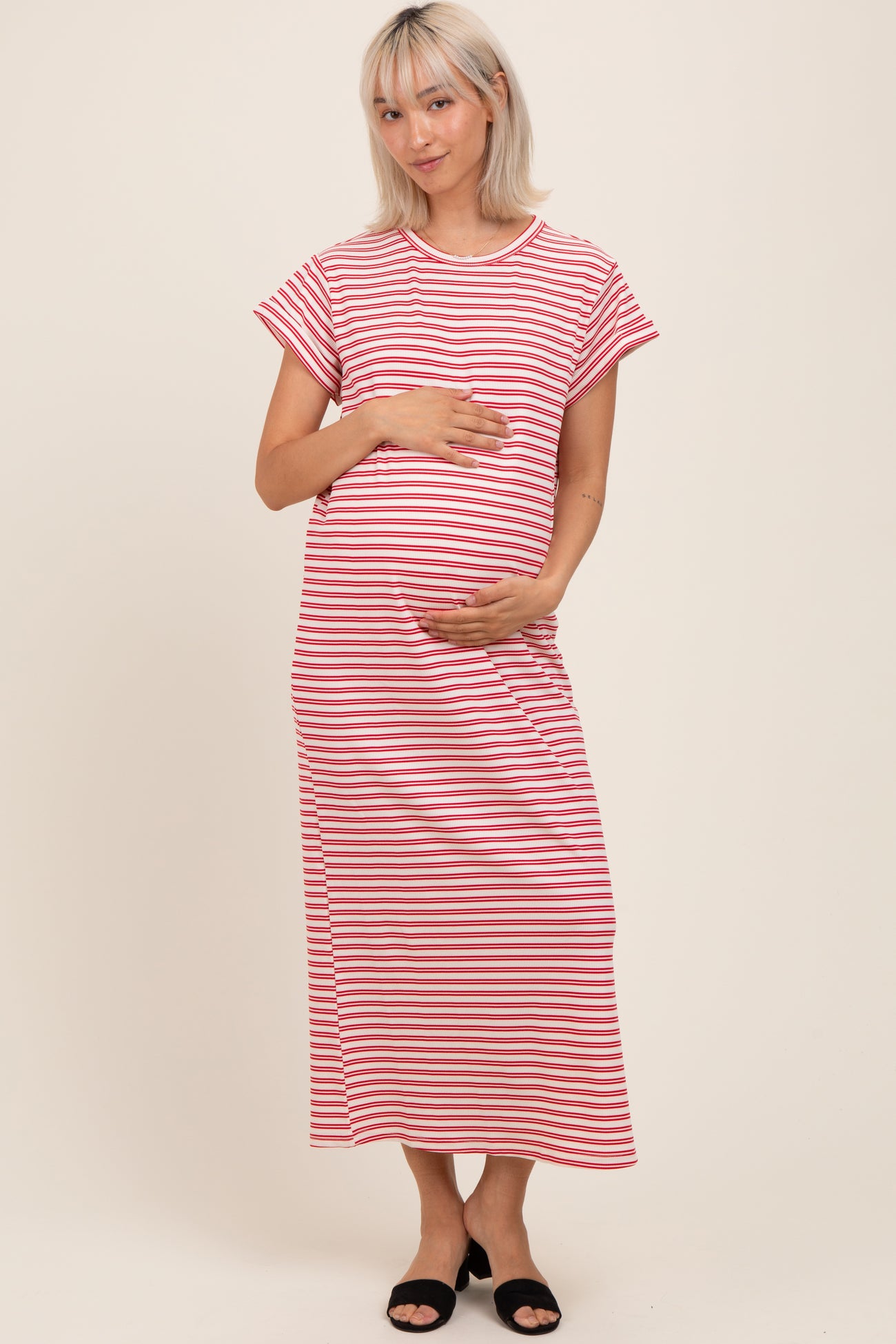 woman wearing a pink and white striped maternity maxi dress and holding her baby bump