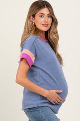 woman wearing a blue striped maternity top with pink accent sleeves and a visible baby bump