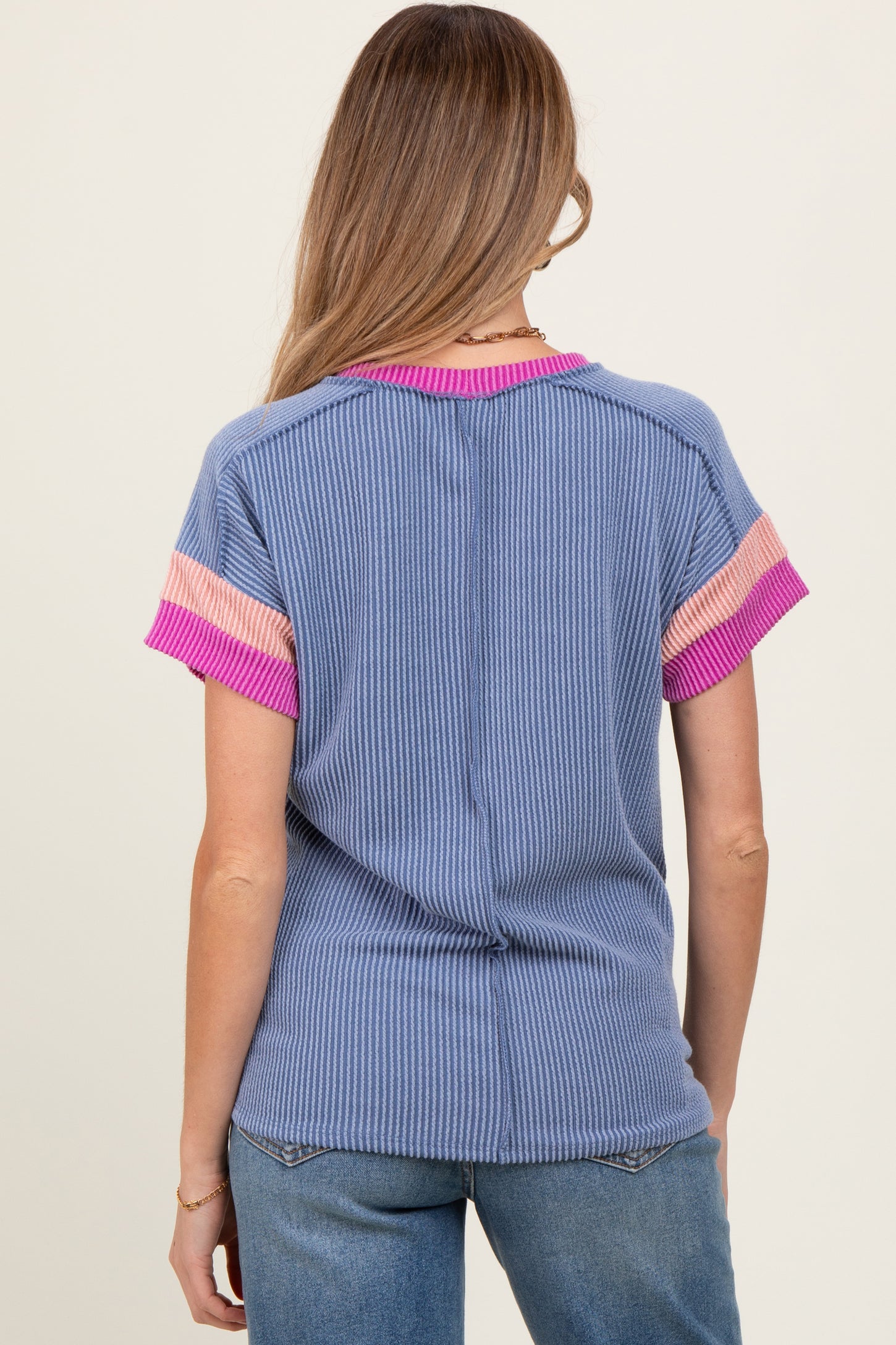 woman wearing a blue ribbed maternity top with pink striped short sleeves and a visible baby bump