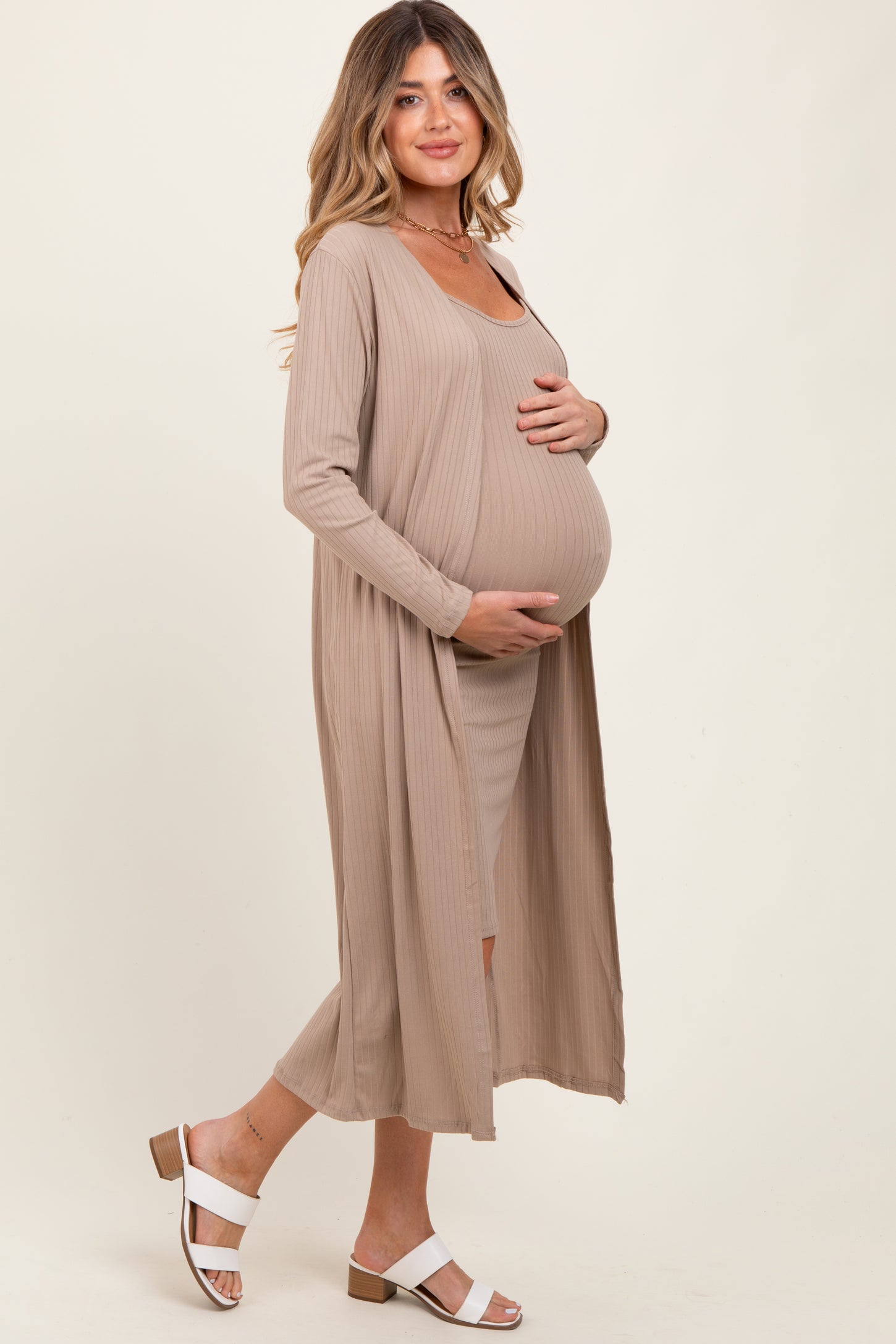 woman wearing a beige maternity dress with a long cardigan and holding her baby bump