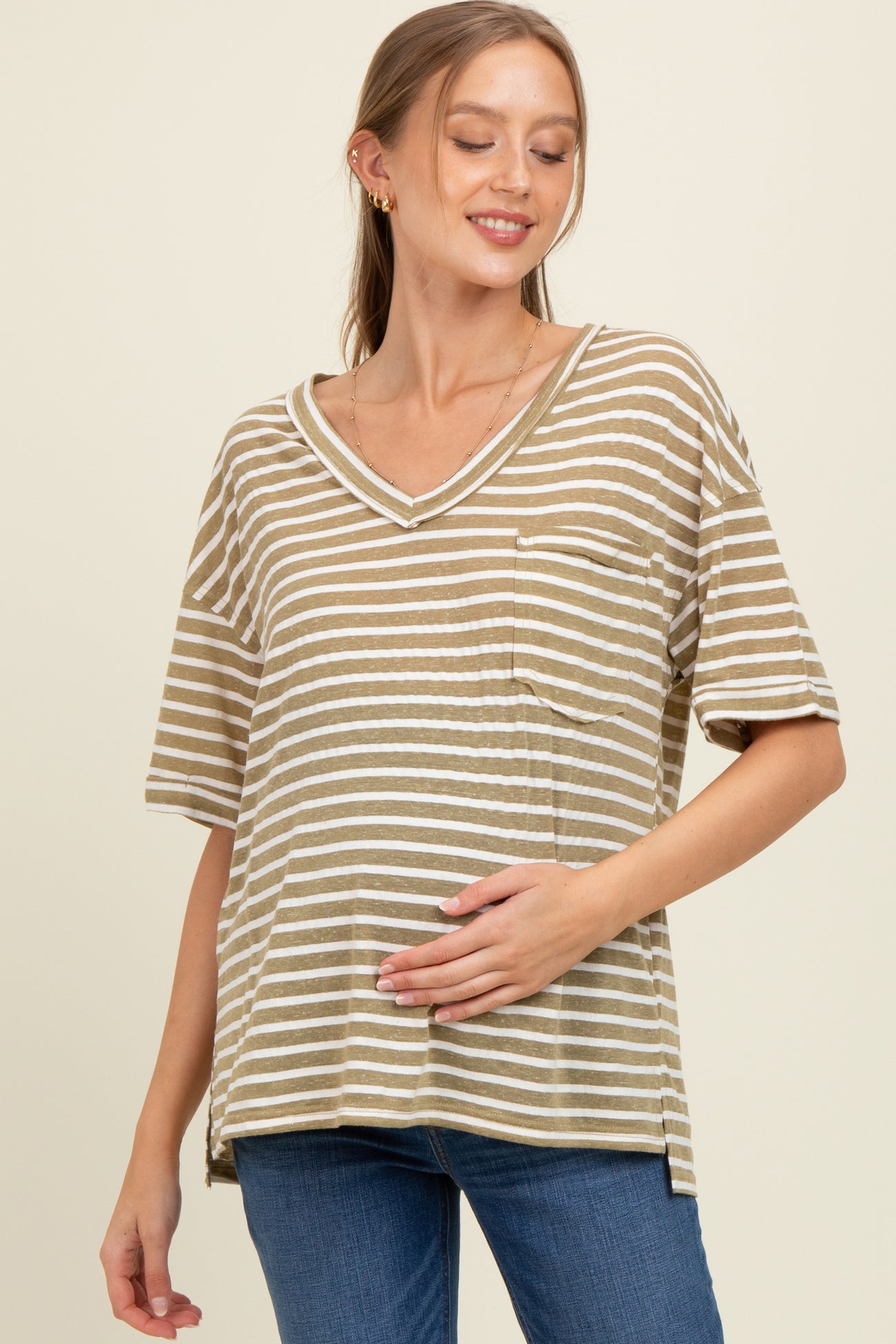 woman wearing a khaki and white striped maternity top with a v-neck and pocket, gently holding her baby bump