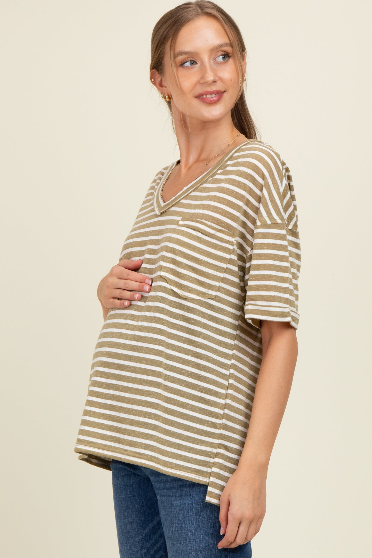 woman wearing a brown and beige striped maternity top and holding her baby bump