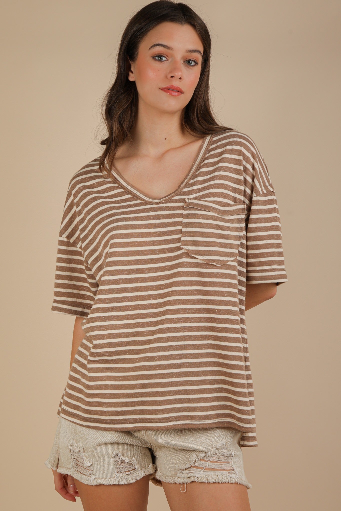 woman wearing a brown and cream striped oversized v-neck t-shirt with a front pocket and distressed white shorts