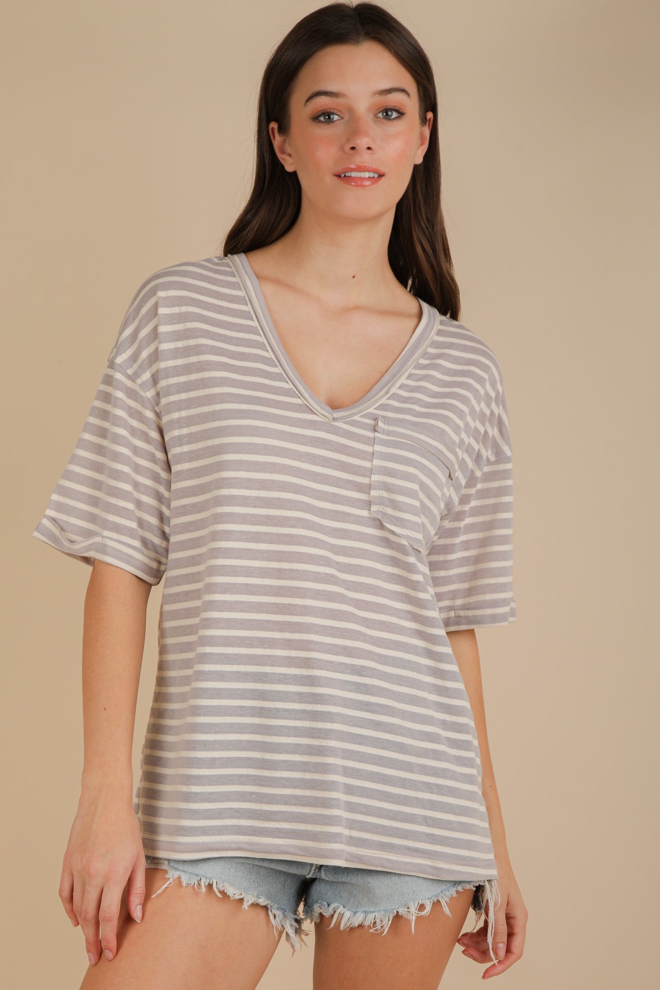 woman wearing a light gray striped oversized v-neck t-shirt with a pocket, paired with distressed denim shorts