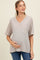 woman wearing a striped beige maternity t-shirt with a v-neck and pocket, holding her baby bump