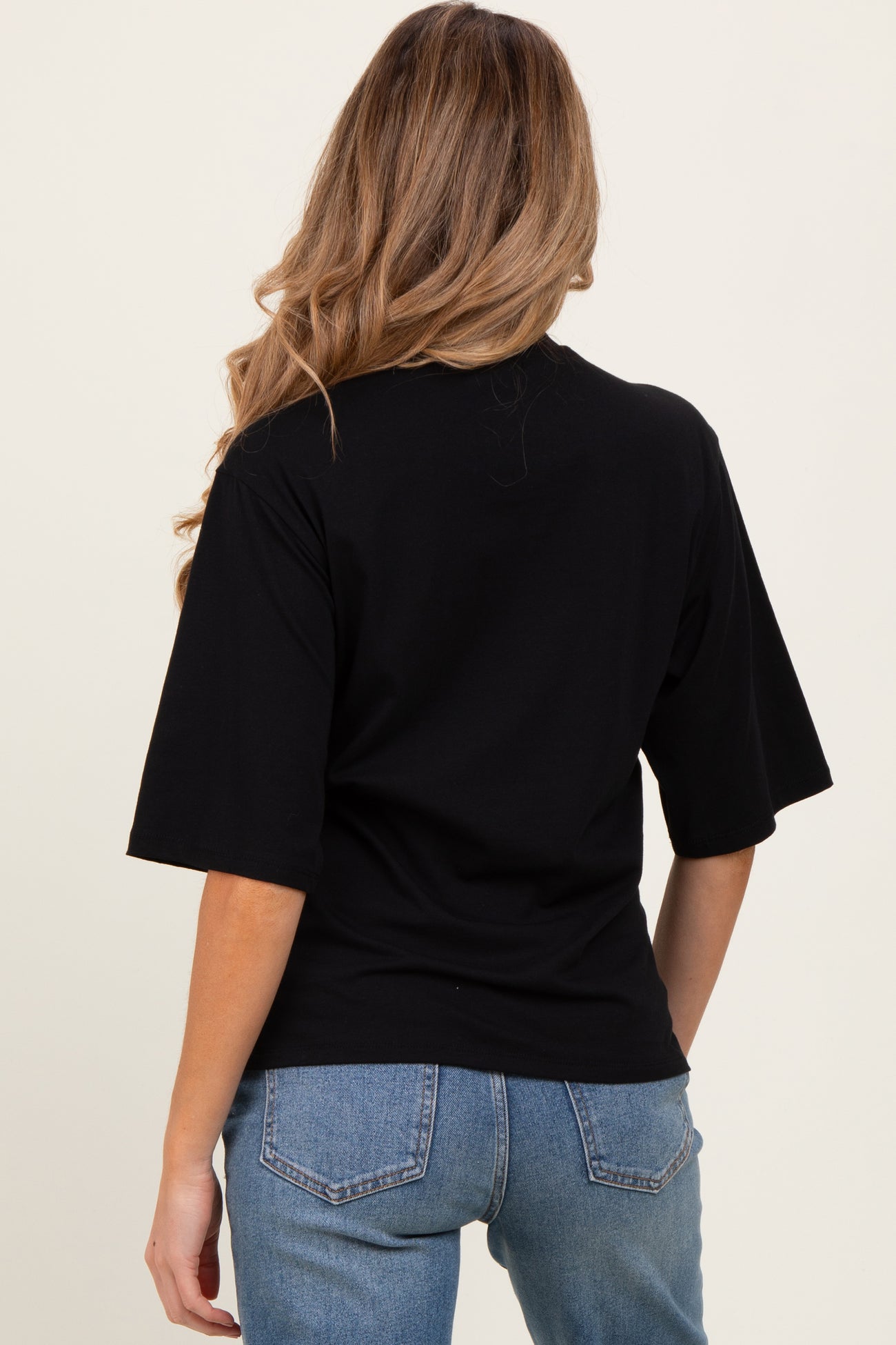 woman wearing a black maternity t-shirt from the back with wide sleeves and styled with denim jeans