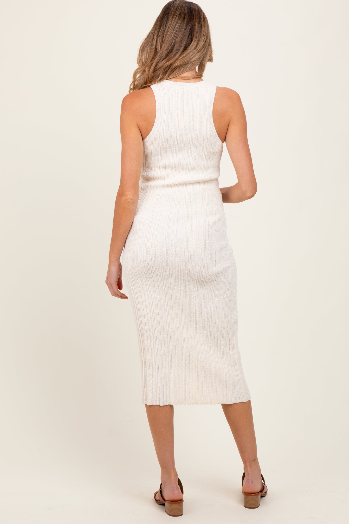 woman wearing a cream ribbed maternity dress with a midi length and fitted style, showing her back